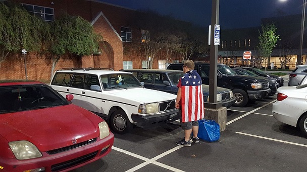 Singer with cape staring at Volvo Station Wagon in Parking Lot